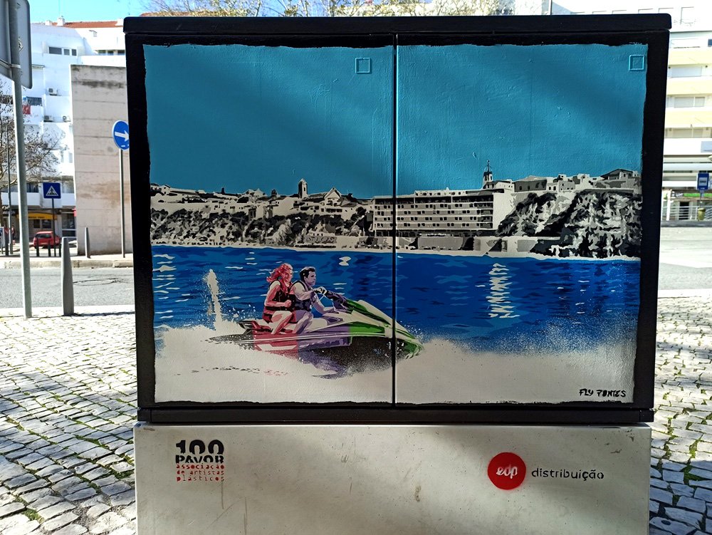 Pintura "Adrenalina da Moto de Água" terminado num armário de electricidade em Albufeira. Um casal em tons fortes desfruta da moto de água, contrastando com o skyline da Praia do Peneco (a cinza). Técnica Stencil e Spray.