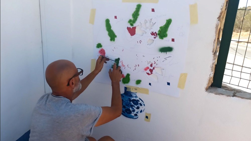 O jarro de porcelana azul está concluído, e o artista Fly Pontes continua a aplicar o stencil para as flores. A imagem mostra a adição das cores verdes e rosas, que darão vida ao bouquet floral exuberante.