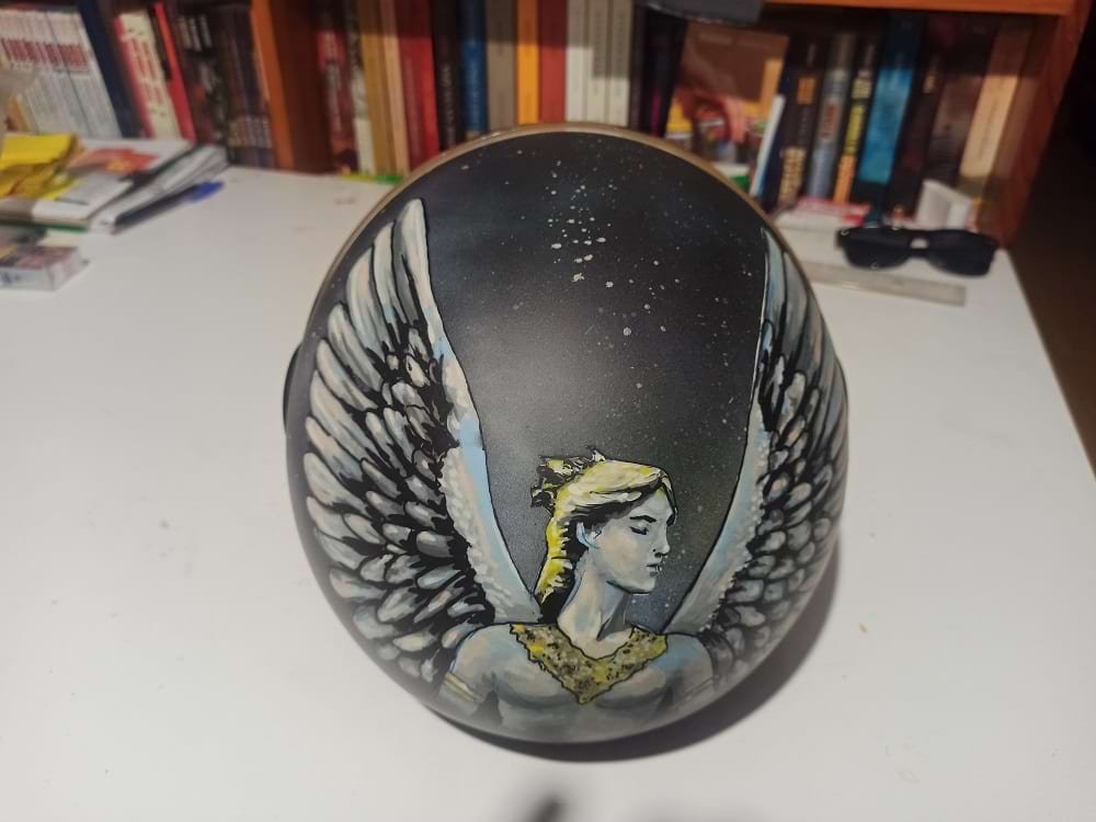 Vista detalhada da parte traseira do capacete, onde se destaca a figura do Anjo com asas abertas, pintada com a precisão dos marcadores Molotow One4all. O design estende-se pela curvatura do capacete.