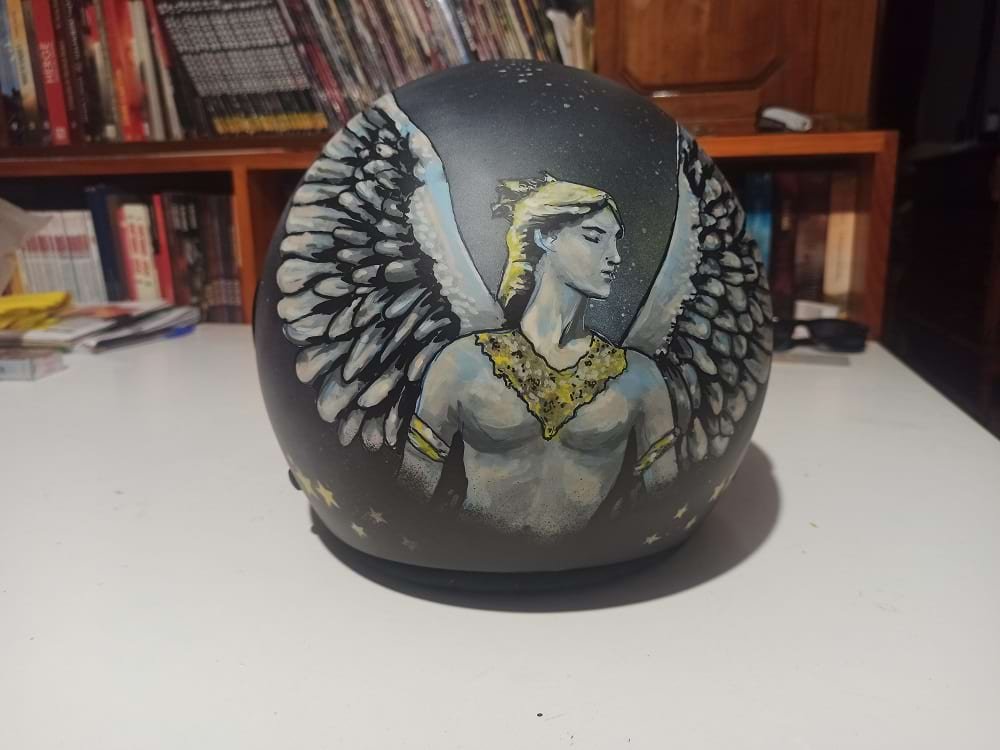 Vista detalhada da parte traseira do capacete, onde se destaca a figura do Anjo com asas abertas, pintada com a precisão dos marcadores Molotow One4all. O design estende-se pela curvatura do capacete.