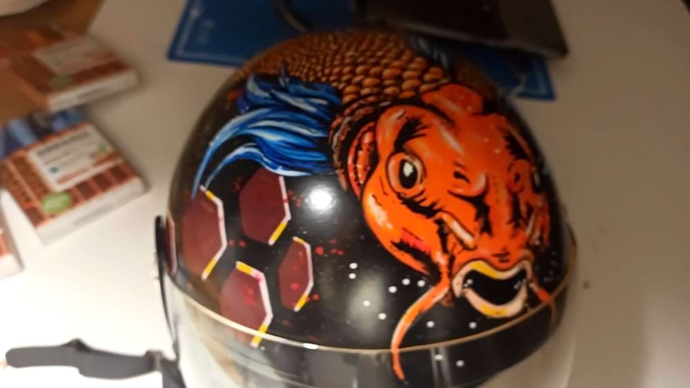 Capacete de mota personalizado com o design de uma Carpa Koi vibrante. O fundo foi criado com spray acrílico e a figura central detalhada com marcadores Molotow One4all, garantindo cores ricas e durabilidade.