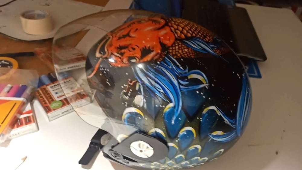 Vista lateral do capacete, mostrando a combinação de técnicas (stencil, spray e marcadores) na composição de fundo e detalhes. Cria uma composição em camadas rica em textura e dinamismo.