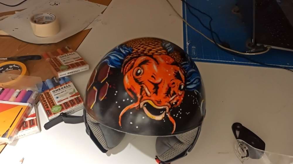 Capacete de mota personalizado com o design de uma Carpa Koi vibrante. O fundo foi criado com spray acrílico e a figura central detalhada com marcadores Molotow One4all, garantindo cores ricas e durabilidade.