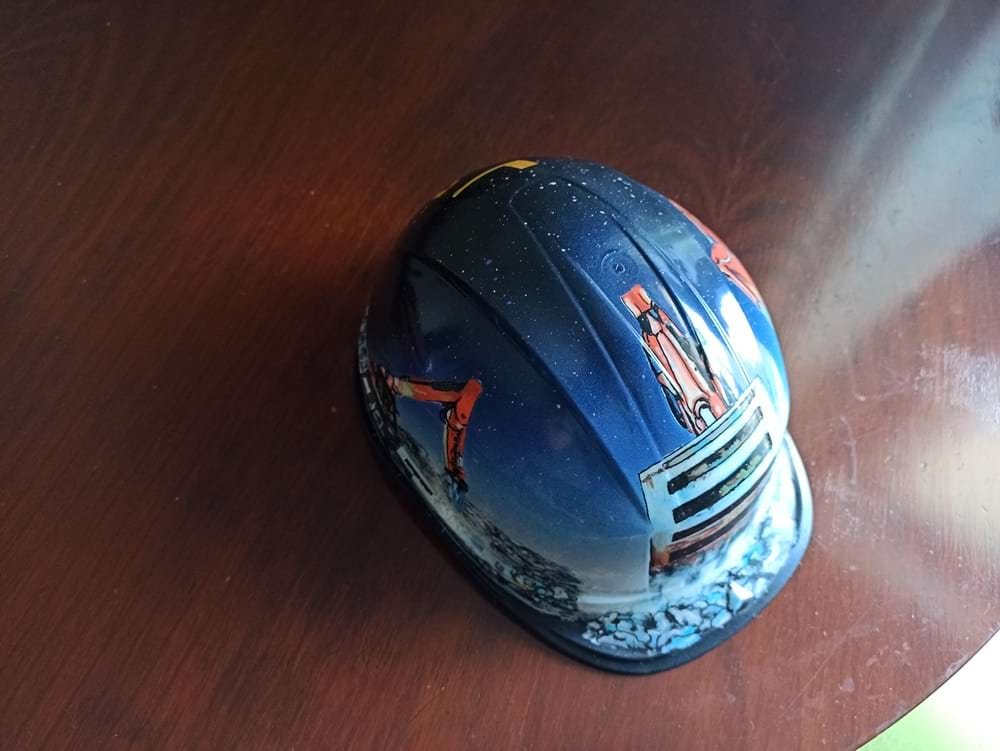 Detalhe da parte de cima do capacete de obra, mostrando a maquinaria pesada específica desenhada para o cliente. A imagem demonstra a precisão dos marcadores na representação técnica.