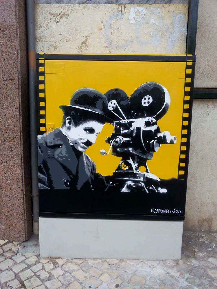 Pintura "Homenagem a Chaplin" terminado em S. B. Messines. Charlie Chaplin e a câmara estão pintados em tons de cinza (cinema mudo) sobre um fundo amarelo vivo. A obra, com autorização da Fundação, é emoldurada por um rolo de filme. Técnica Stencil e Spray.
