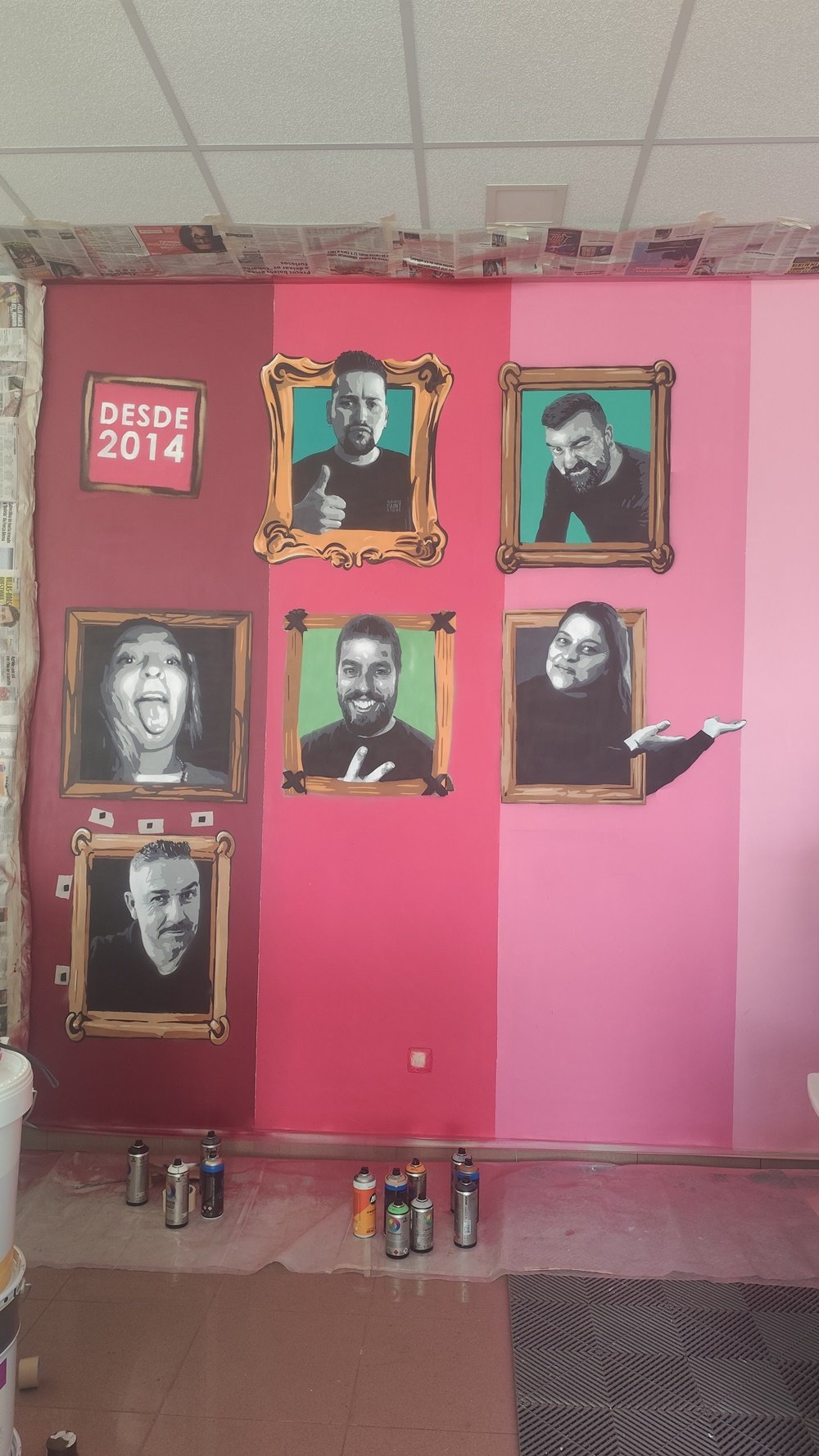 Mural para a Algarve Paint Store a meio da pintura. Já se veem seis retratos de colaboradores em Stencil, com o fundo rosa e a moldura com o ano de 2014 (ano de inauguração da loja) visível. Documentação do processo em Ferreiras.