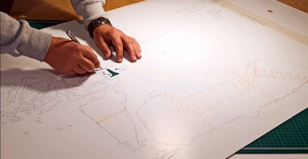 O artista Fly Pontes no estúdio, a cortar o stencil com um bisturi, preparando as camadas para a pintura "O Autocarro no Largo da Meia Laranja". Este trabalho manual é crucial para a precisão dos detalhes do autocarro e da arquitectura.