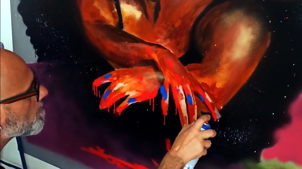 Detalhe das mãos da bailarina com salpicos e tinta nas pontas dos dedos em azul e vermelho. O corpo da figura está em tons castanhos (base). Este contraste realça o movimento e a expressão cromática da dança no mural.