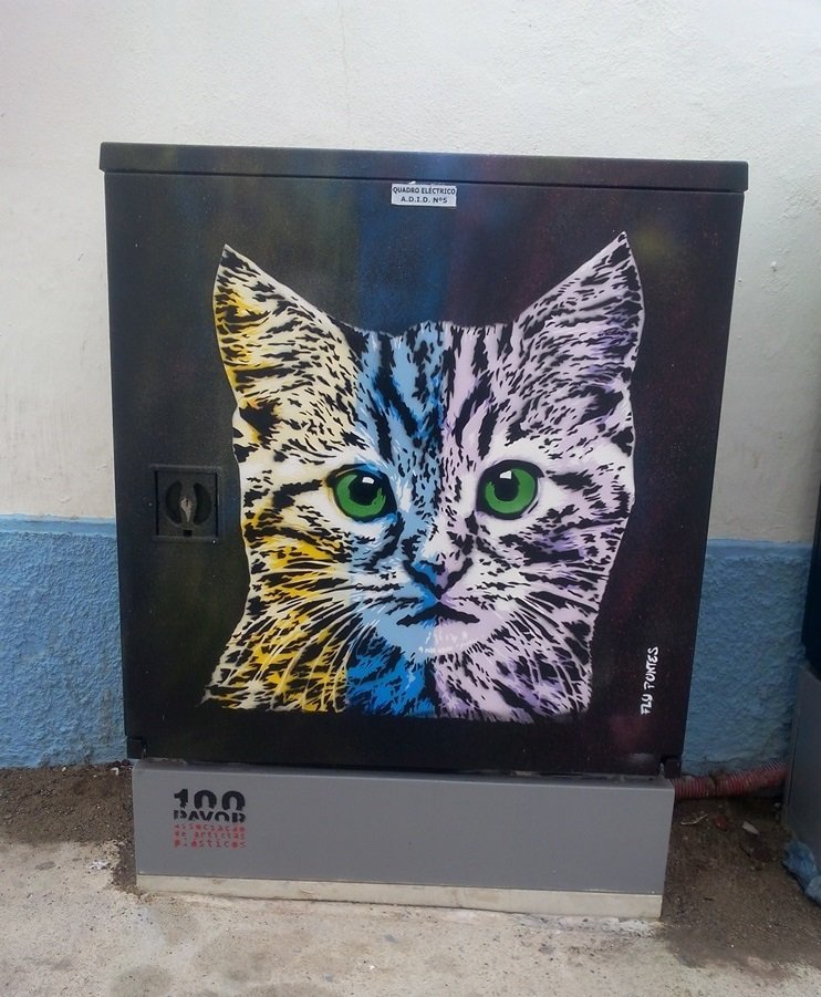 Pintura "O Gato Pop" terminado num armário de electricidade em Albufeira. O gato, em amarelo, azul e violeta, contrasta vivamente com o fundo preto. A obra é uma homenagem cromática ao estilo do artista Kobra.