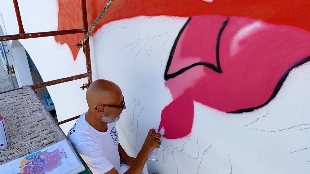 Início da pintura do mural "A Metamorfose" com vista de cima do andaime. O artista Fly Pontes está a pintar o cérebro de cor de rosa, um dos lobos cerebrais que simbolizam a evolução na obra da USO.