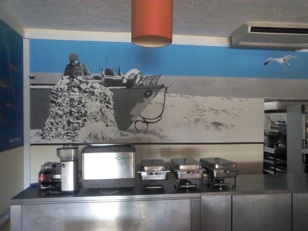 Vista do lado esquerdo do mural de Armação de Pêra. O segundo Pescador está junto ao monte de redes e ao Barco. A cena, em tons de cinza da memória, é emoldurada pelo céu azul vibrante e completada por uma Gaivota a voar.