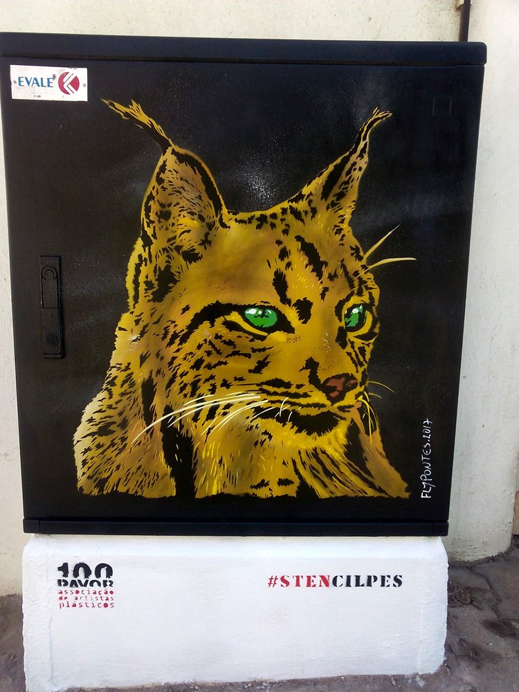 Pintura "Lince Ibérico" terminado em S. B. Messines. O lince está pintado em tons quentes de amarelo e ocre sobre um fundo preto, com olhos verdes intensos. Homenagem à conservação da espécie em Messines. Técnica Stencil e Spray.