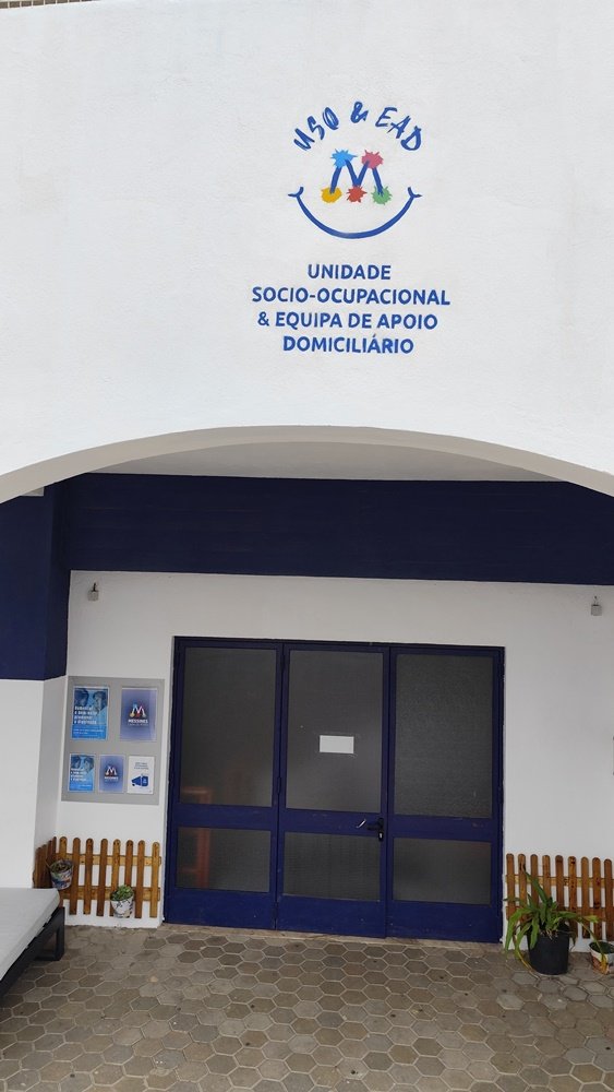 Pintura final do logotipo da Unidade Sócio-Ocupacional (USO) por cima da entrada do pavilhão. O logotipo complementa o mural "A Metamorfose", reforçando a identidade da instituição. Arte urbana de branding.