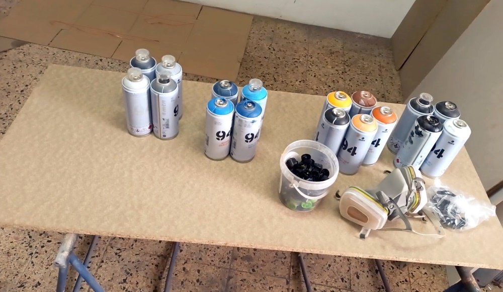 Materiais de Arte Urbana prontos para o mural: latas de spray de diversas cores, várias caps (bicos) para diferentes traços e a máscara de protecção, essenciais para o trabalho técnico em grande formato.