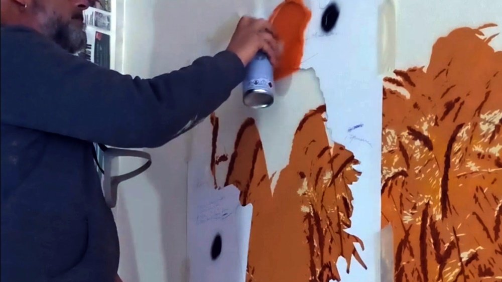 O artista Fly Pontes a pintar uma das camadas de stencil das figuras das Ceifeiras no mural. A técnica de stencil permite a criação precisa dos contornos e detalhes das ceifeiras em plena colheita no campo.