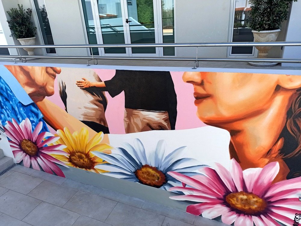 Mural "Afecto e Cuidado em Lar de Idosos" (2021) na entrada da instituição. A pintura celebra o laço humano entre cuidadores e utentes com figuras simbólicas e flores vibrantes, criando um ambiente acolhedor.
