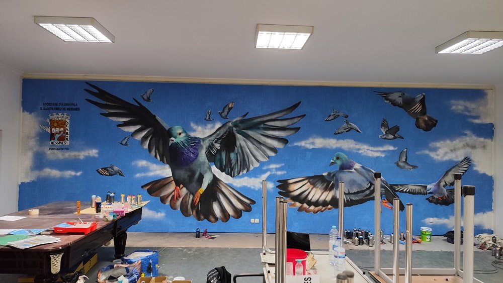 Mural Columbofilia terminado na Sociedade Columbófila Messinense. A imagem mostra a obra de arte urbana concluída com todas as tintas e material de pintura espalhados pela sala, evidenciando o processo intenso de criação.