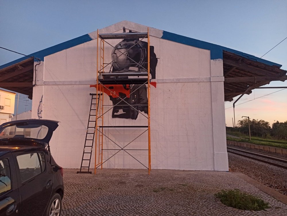 Andaimes colocados a meio da parede da estação Almancil - Neche (Esteval). A locomotiva principal do mural já está pintada. Foto de arte urbana em progresso.