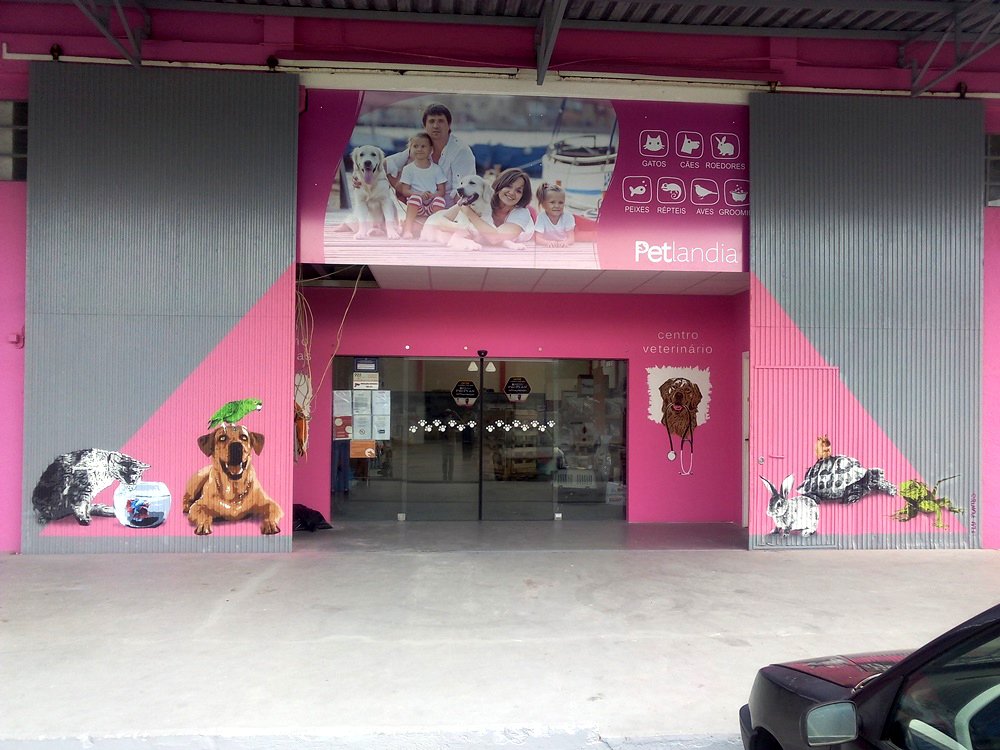 Mural no Portão de Entrada da Petlandia, Albufeira (em stencil e spray). A obra celebra a fauna da loja (Gato, Papagaio, Cão, Rato e Tartaruga) num fundo cor de rosa, com um efeito dinâmico que se integra na parede interior quando o portão está aberto.