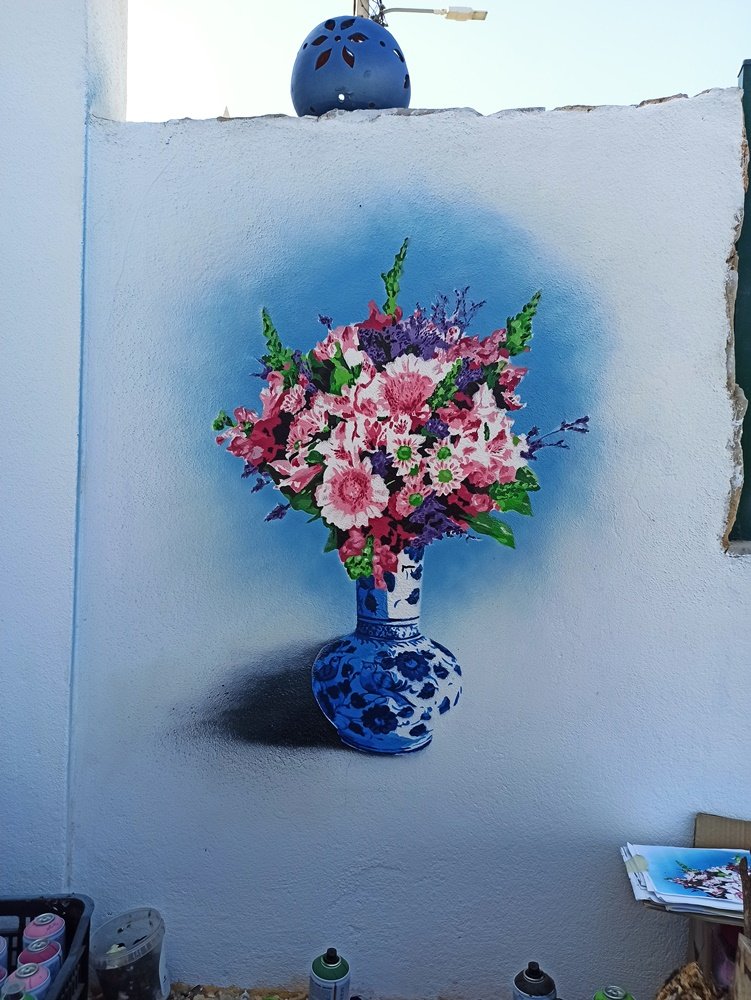 Pintura "Natureza Morta em Stencil" quase pronto, faltando apenas pequenos retoques e a assinatura. Uma vista afastada mostra latas de spray e a imagem de referência pousada no muro.