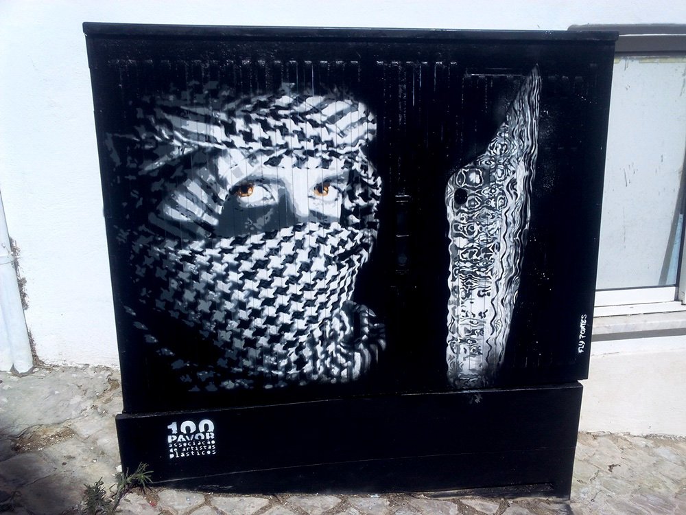 Pintura na Mouraria de Albufeira, em homenagem aos mouros. A figura, pintada integralmente em tons de cinza, revela apenas os olhos, com a adaga detalhada a contrastar, evocando o mistério e as raízes da cidade.