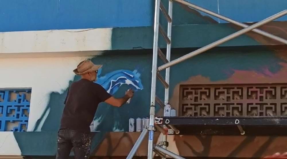Artista Fly Pontes pintando o mural de conservação marinha Pedra do Valado, em Armação de Pêra.