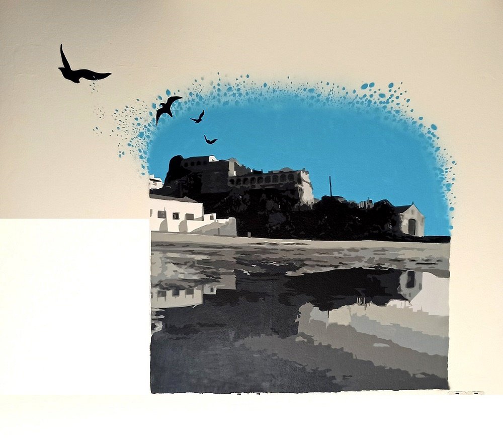 Pintura na Padaria A Ceifeira (Milfontes) com a silhueta do Forte de Milfontes em destaque. A vista do mar para terra em tons cinzentos e azul cria uma atmosfera nostálgica. Pássaros em silhueta voam, adicionando dinamismo.