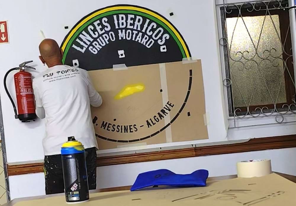 Artista a pintar o logótipo estilizado dos Linces Ibéricos GM no restaurante, utilizando stencil.