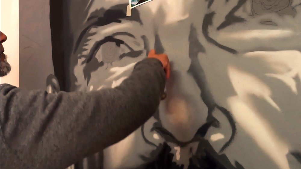 O artista Fly Pontes a pintar a zona do nariz do retrato. A aplicação dos tons cinza já revela os claros e escuros, essenciais para dar volume e forma realista à face, mantendo o estilo monocromático da figura.