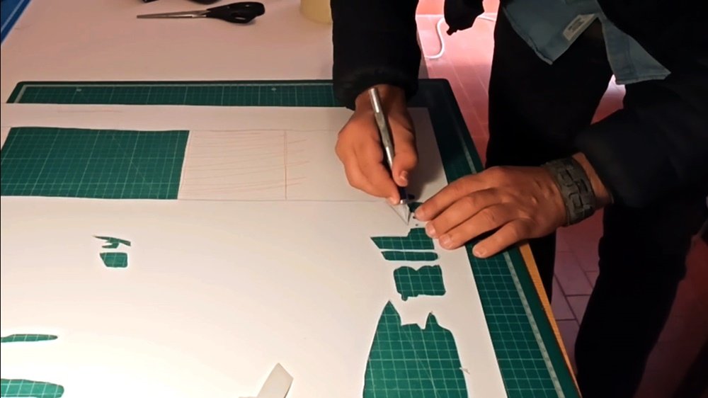 O artista Fly Pontes no estúdio, a cortar uma das camadas do stencil com um bisturi. Este trabalho manual é a fase de preparação meticulosa para a pintura "A Última Taberna de Albufeira", garantindo a precisão dos detalhes.