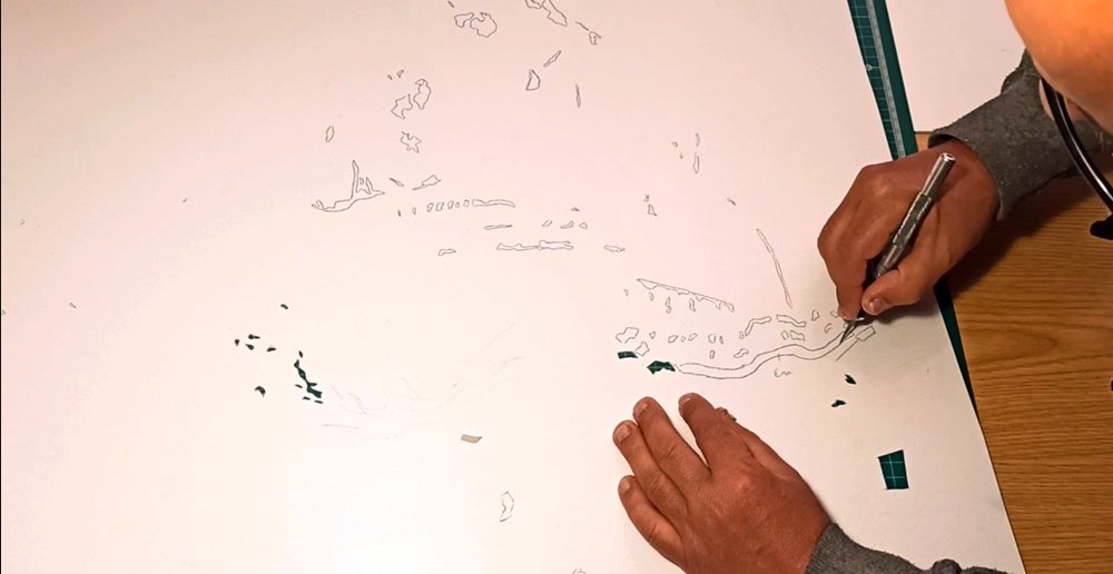 O artista Fly Pontes no estúdio, a cortar o stencil com um bisturi, preparando as camadas para a pintura do Rancho Folclórico. Este trabalho manual meticuloso é crucial para a precisão dos trajes e figuras históricas.