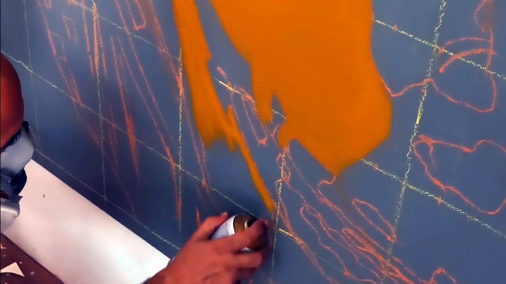 Início da pintura do mural "Estudo de Cor e Escala". O artista aplica as primeiras linhas com spray sobre a quadrícula e as linhas guia, que asseguram a proporção e a precisão do retrato em grande plano.