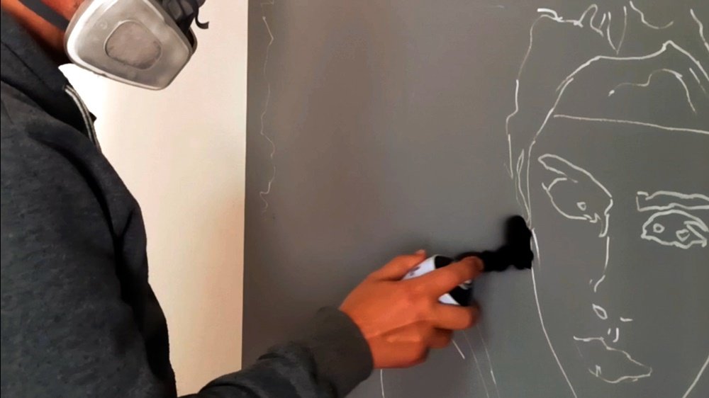 Início da pintura do mural "A Graça das Bailarinas". O artista aplica a primeira linha de spray sobre as linhas guias da figura, definindo a forma inicial do estudo de movimento em grande formato.