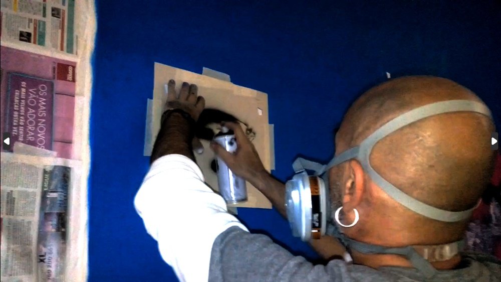 O artista Fly Pontes a pintar um dos peixes do mural "O Ecossistema Marinho Local", utilizando a técnica de stencil. O stencil permite a criação de formas e texturas precisas dos peixes, que habitam o coral detalhado.