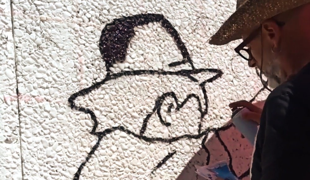 O artista Fly Pontes a traçar as primeiras linhas a preto no mural do Rancho Folclórico. O artista segura a imagem de referência na mão, garantindo a precisão da homenagem à tradição da cultura local de Almancil.