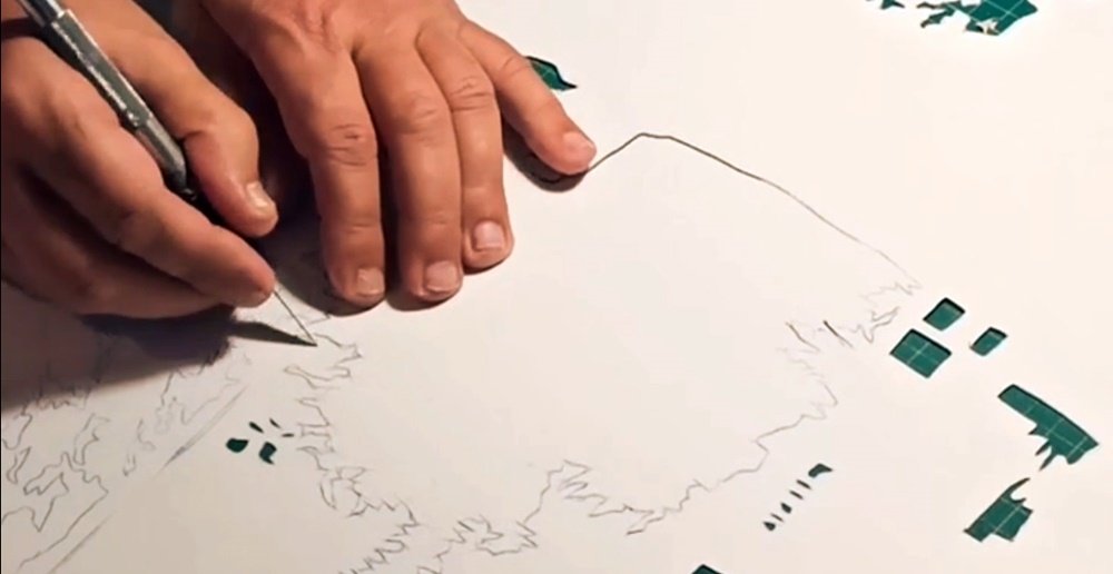 O artista Fly Pontes a cortar o stencil com um bisturi, preparando as camadas para a pintura "O Resgate da Feira Franca". Este trabalho manual meticuloso é crucial para a precisão dos detalhes das figuras e objectos históricos.