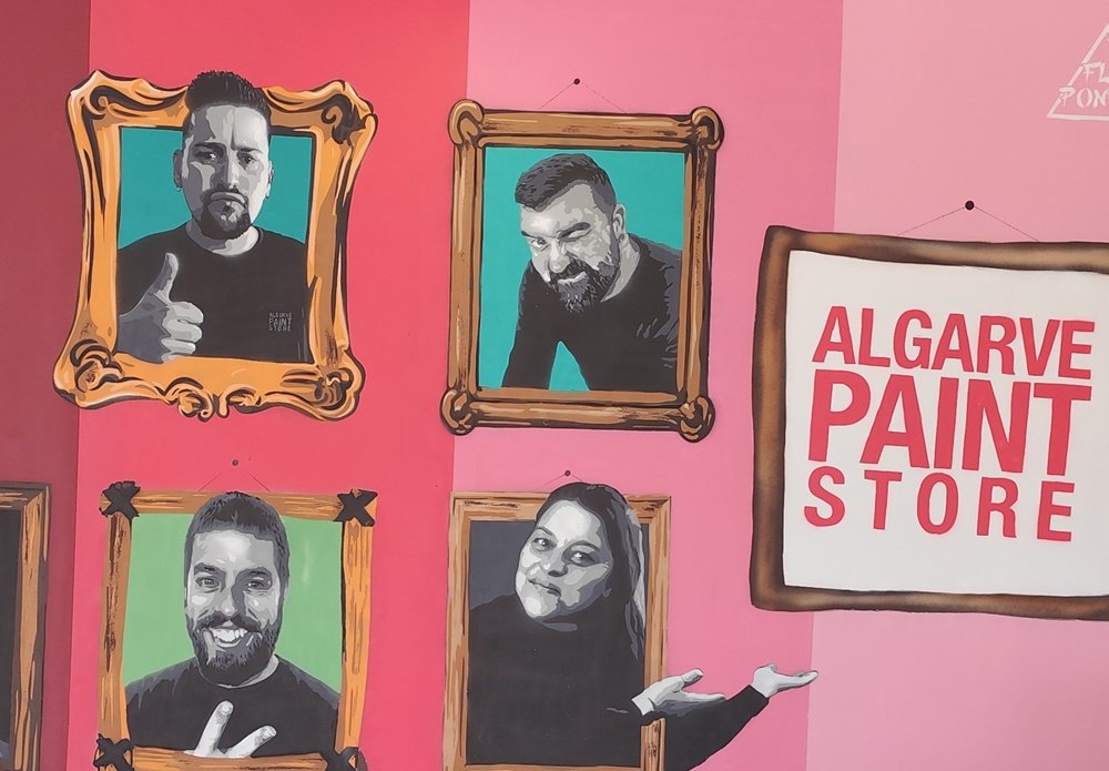 Pormenor de quatro retratos de trabalhadores (incluindo os donos) no mural da Algarve Paint Store. As figuras em cinza saem das molduras castanhas. O fundo da moldura é verde e o fundo do mural é rosa, integrando as cores institucionais da marca.