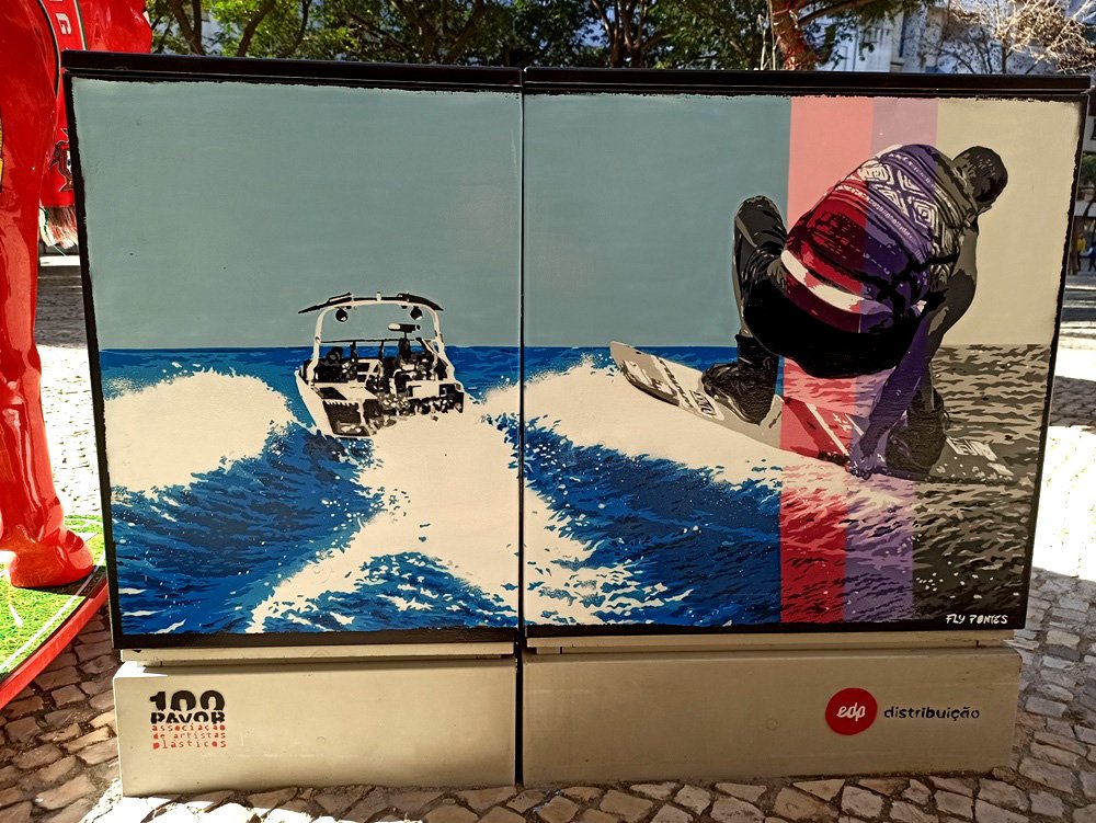 Pintura "Adrenalina Aquática: Ski Aquático" terminado num armário de electricidade em Albufeira. A figura do esquiador salta uma onda, pintada em tons de cinza para contrastar com a água azul viva. Foco no movimento e velocidade.