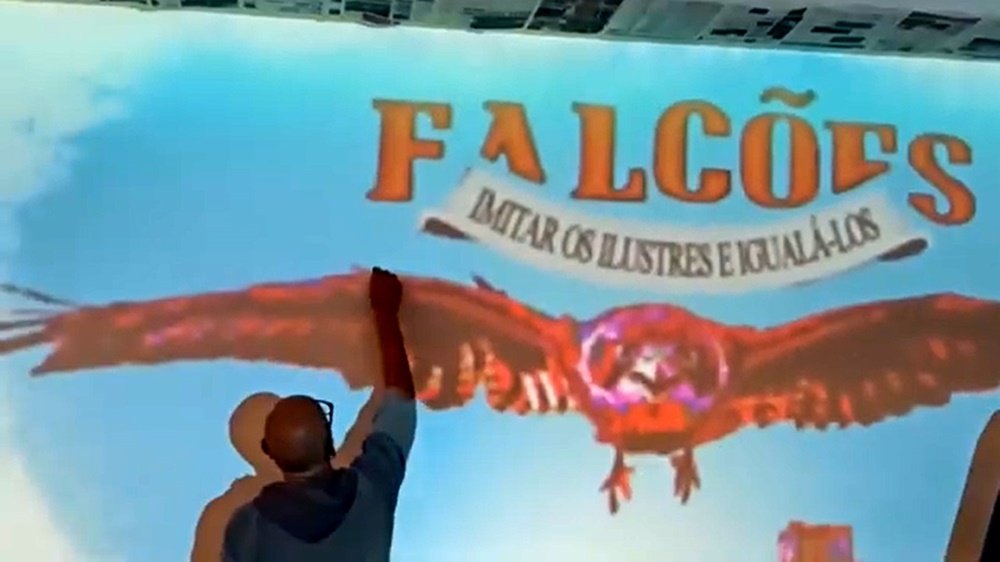 O artista Fly Pontes a traçar, com lápis de carvão, apenas as linhas mestras do Falcão no mural da BA11. A imagem projectada ajuda a definir o posicionamento do Falcão (a ser pintado a pincel), do Castelo de Beja e do logotipo (ambos aplicados com stencil).