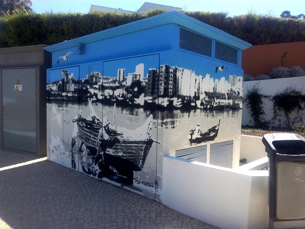 Canto do posto de transformação mostrando a transição entre as duas vistas do mural. O fundo com Portimão dá a ilusão de continuidade, unindo a cena dos pescadores a puxar o barco e a cena do pescador no barco. Destaque para a ilusão óptica da dupla vista.