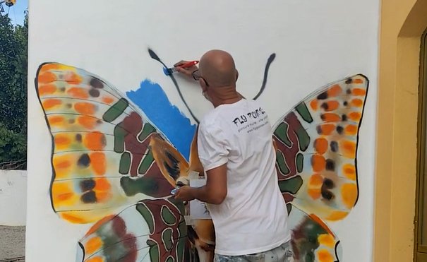 Artista Fly Pontes a pintar mural de uma girafa com asas de borboleta em parede exterior.
