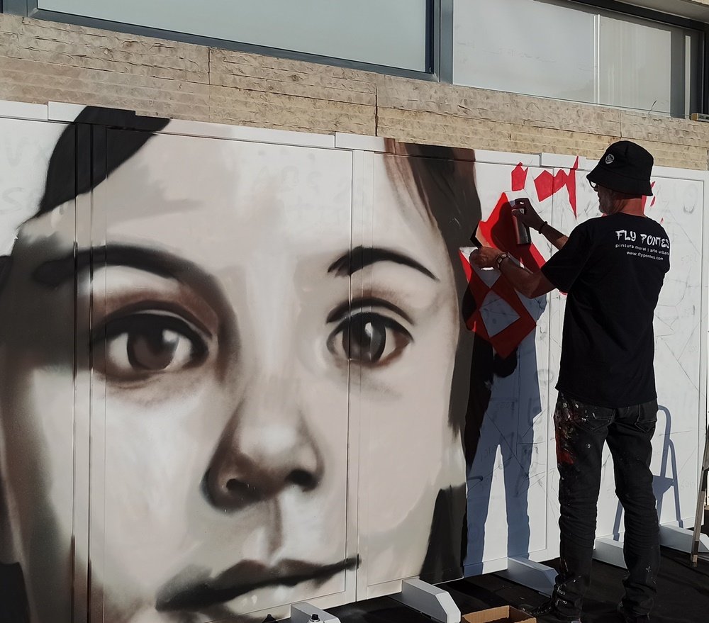 Artista a pintar pétalas geométricas num cravo vermelho junto ao rosto realista da criança.