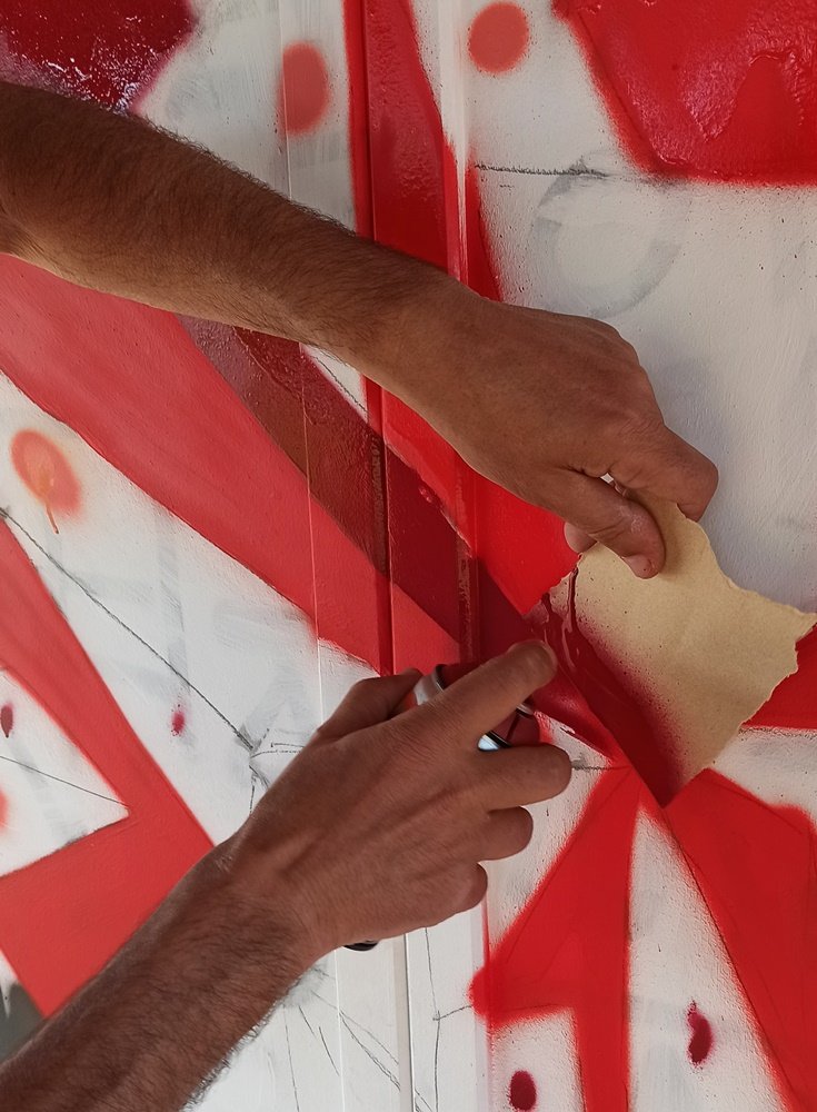 Grande plano da mão do artista a segurar cartolina e a aplicar spray num ângulo geométrico.