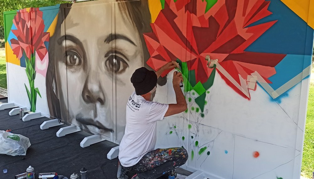 Mural quase completo com rosto e cravos terminados, mas com espaços geométricos vazios para participação do público.