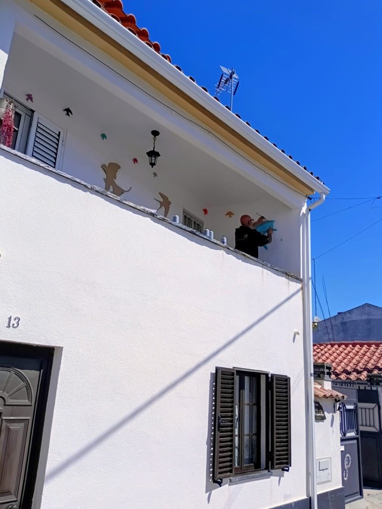vista de rua do artista a trabalhar no preenchimento do céu azul na parede lateral da varanda.