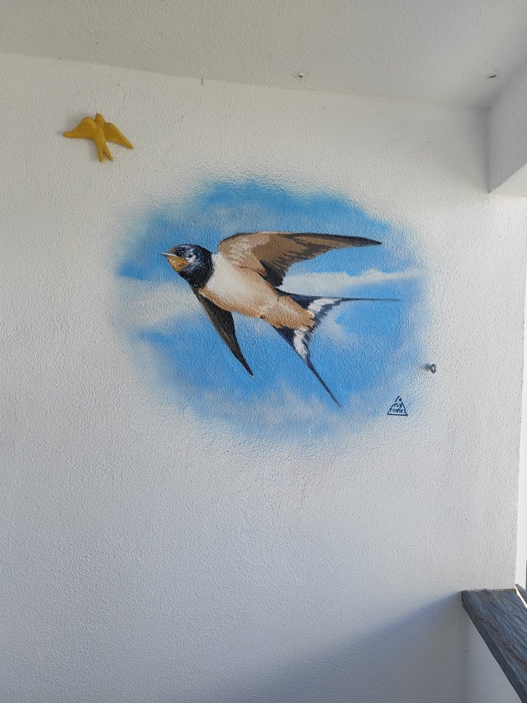 pintura de uma andorinha a voar num céu azul com nuvens brancas numa parede de varanda.