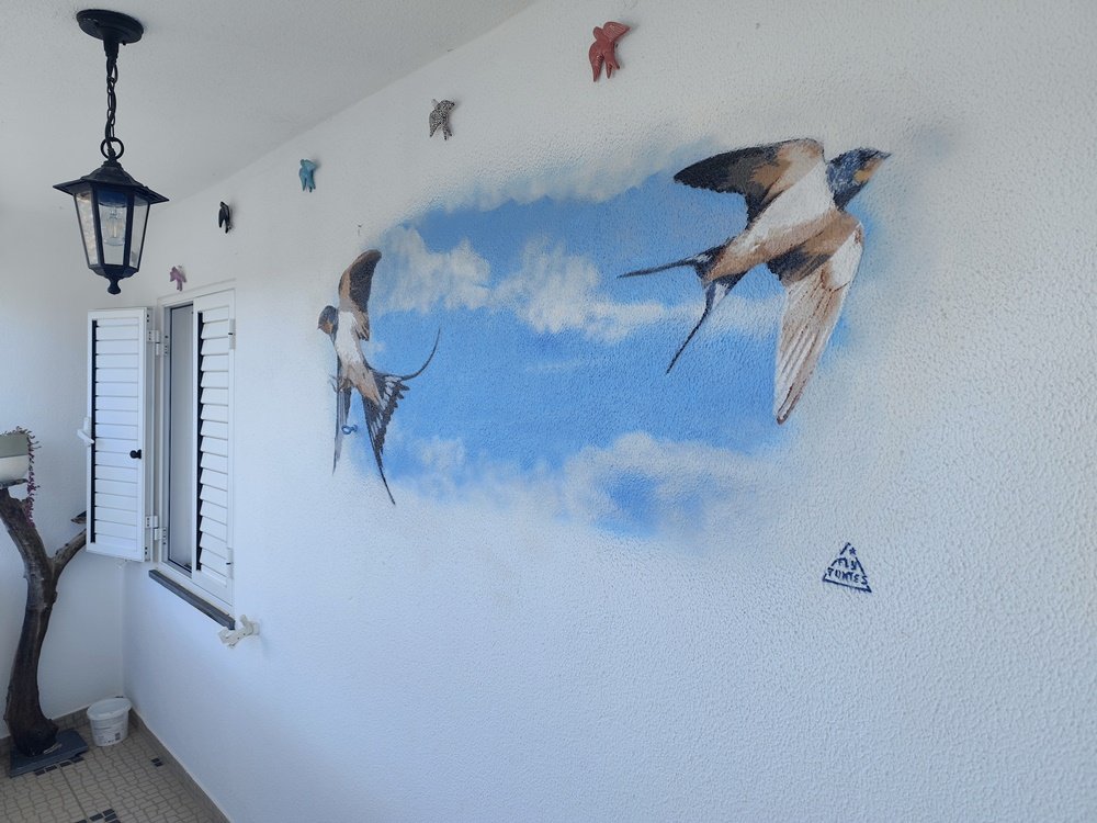 duas andorinhas pintadas a voar em direcções opostas parecendo sair dos limites do mural azul.