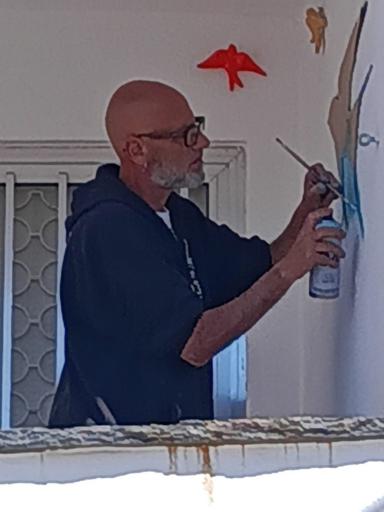 detalhe das mãos do artista a segurar um molde de papel contra a parede com o auxílio de um pequeno pau de madeira.