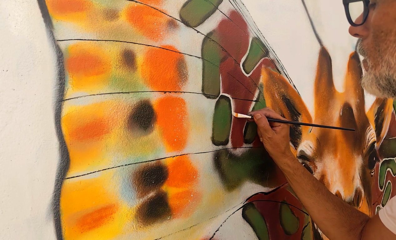 O artista Fly Pontes no andaime a pintar com pincel os contornos pretos e brilhos brancos no olho realista da girafa.