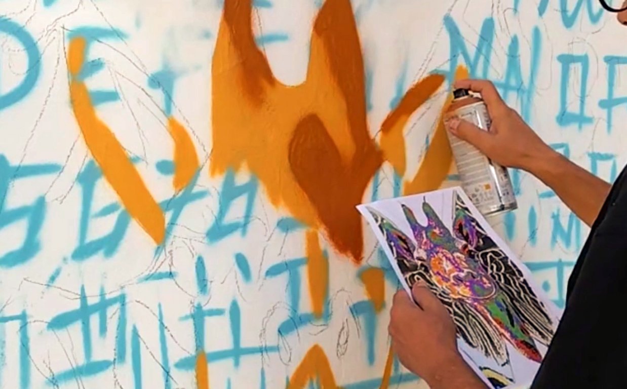 Linhas iniciais e blocos de cor bege e castanha pintados a spray na parede, delineando o início do rosto da girafa.